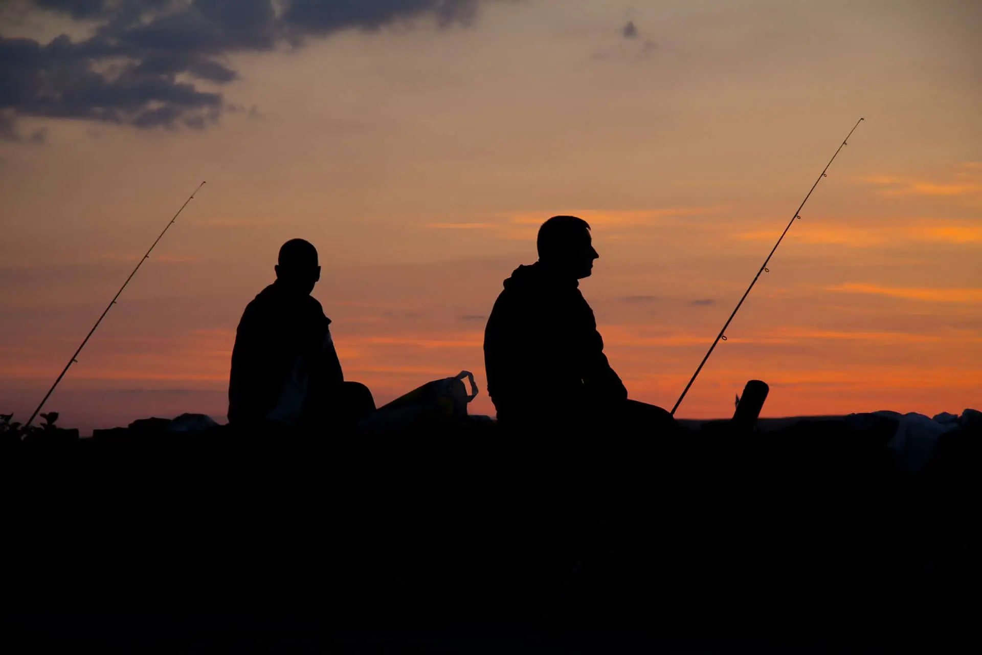 Zwei Angler sitzen bei Sonnenuntergang mit ihren Angeln an einem See