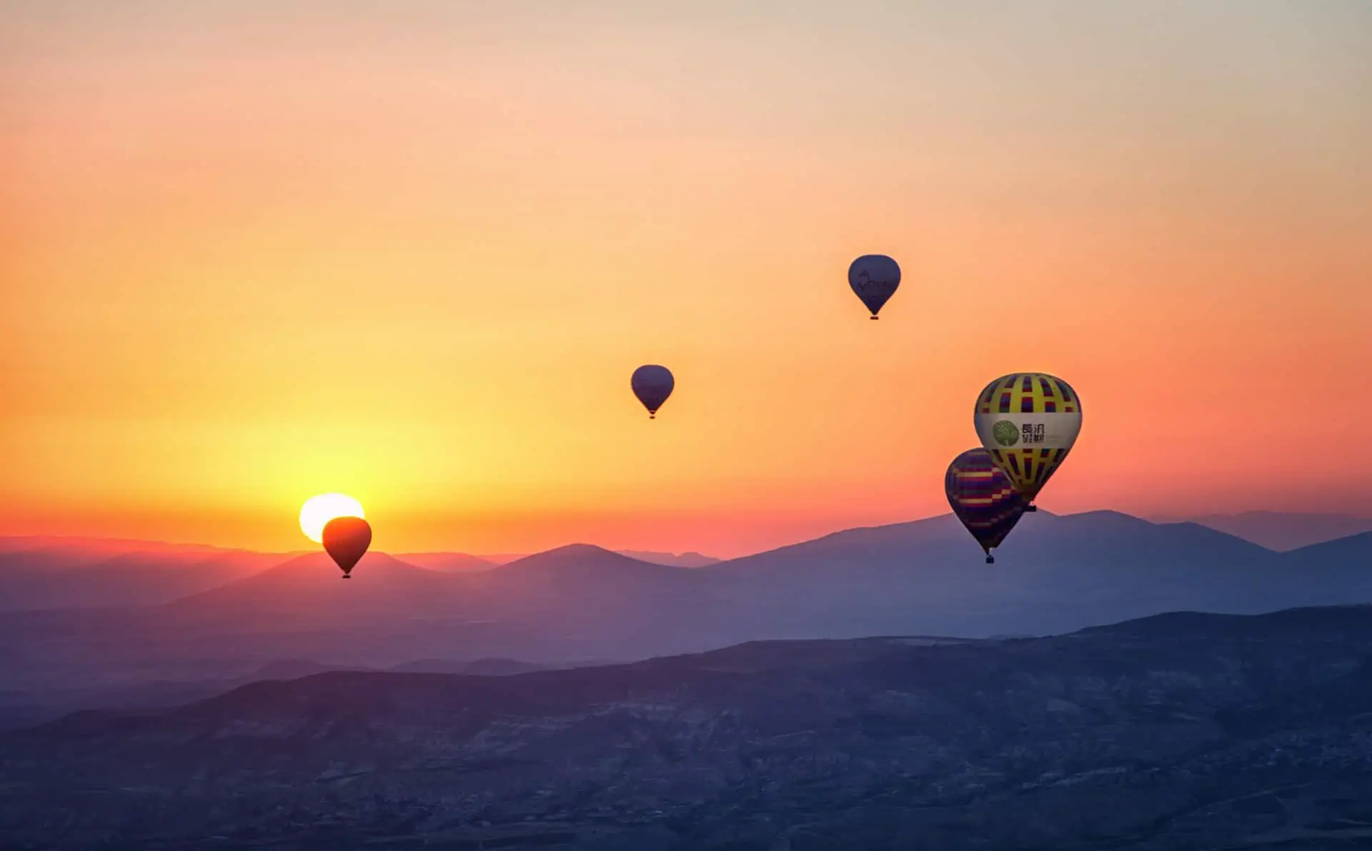 Fünf Heißluftballons fahren über hügelige Landschaft im Sonnenuntergang
