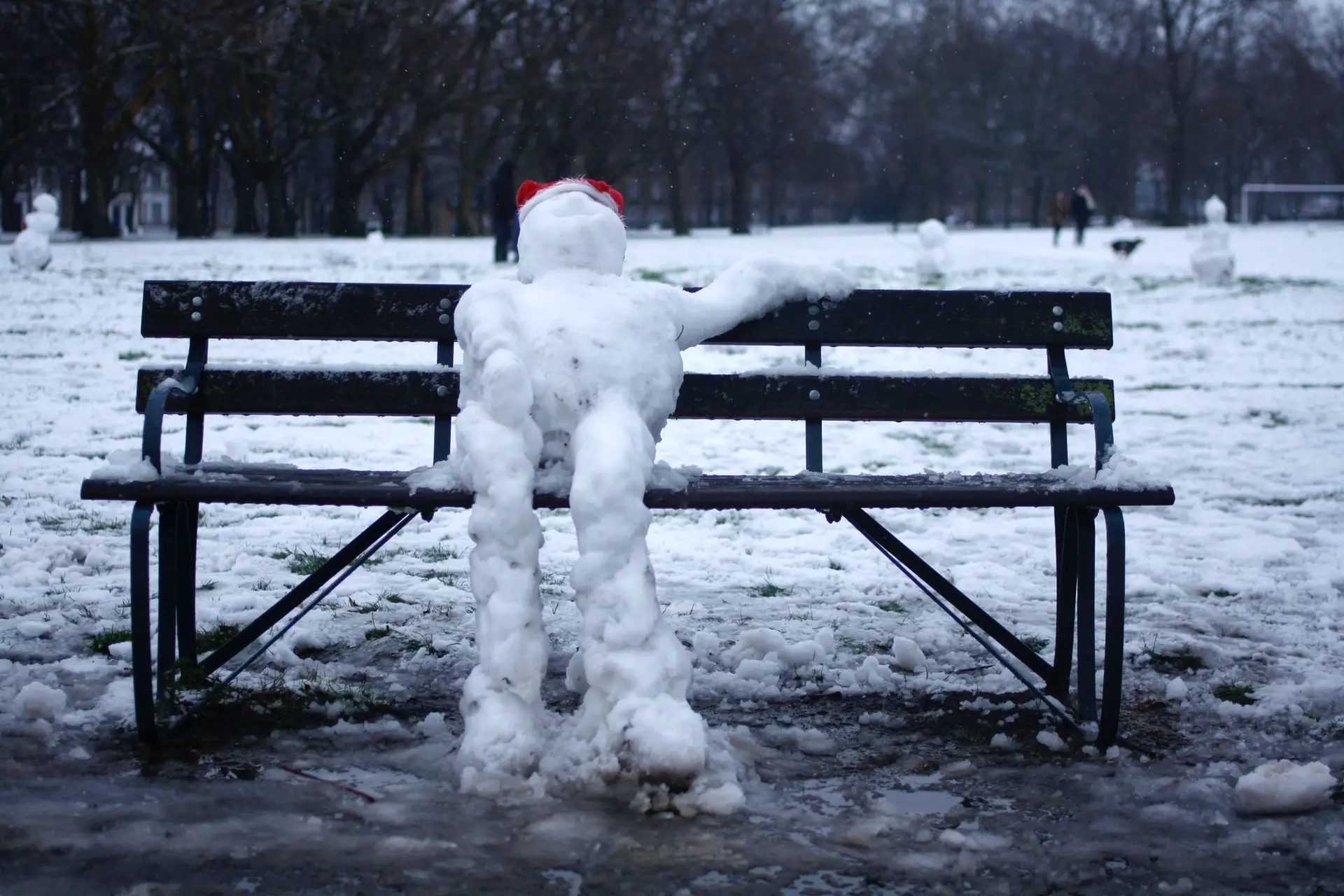 Ein schmelzender Schneemann sitzt auf einer Parkbank